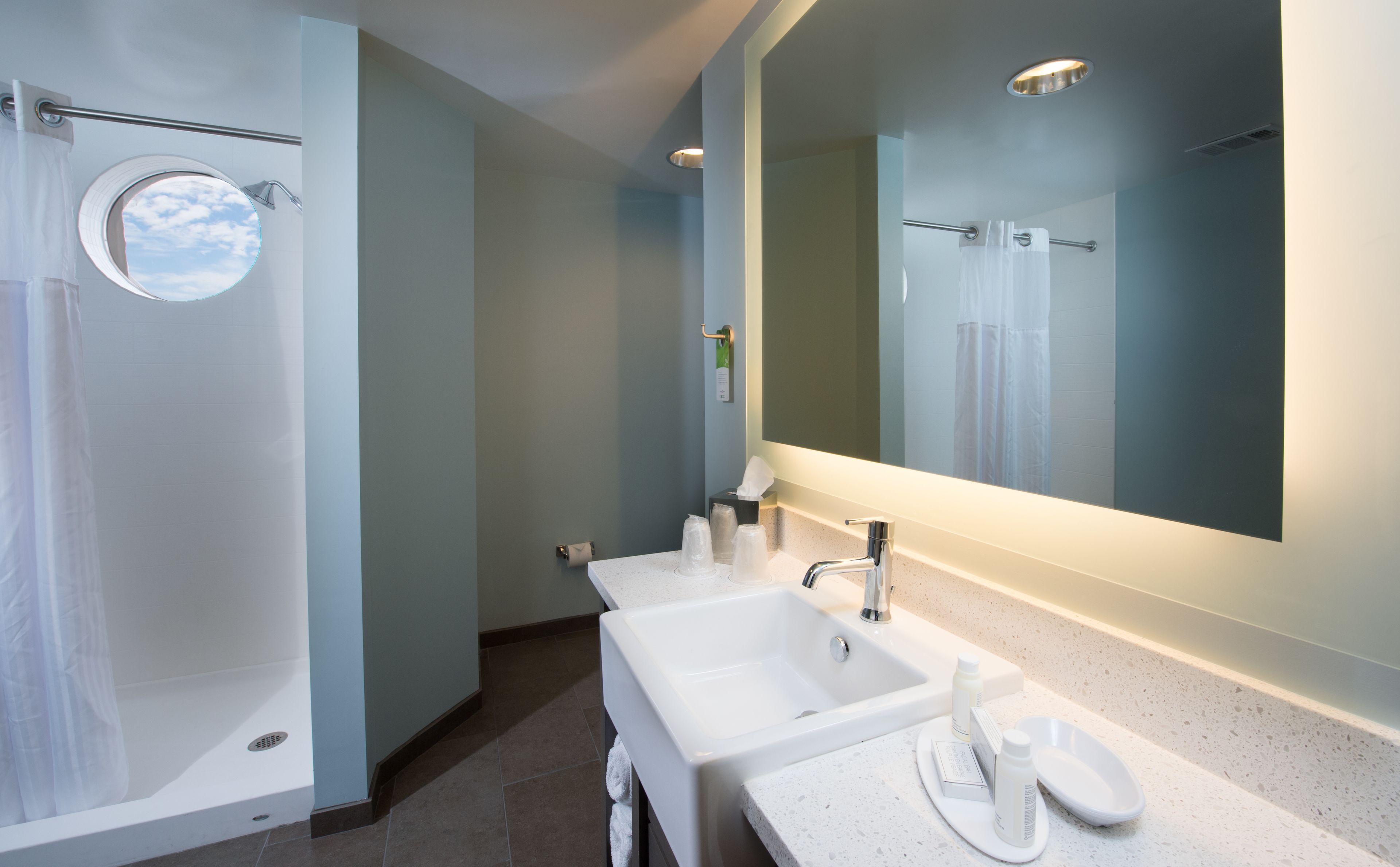 Un baño moderno con ducha a ras de suelo, dos lavamanos, un espejo grande y un perchero para toallas.