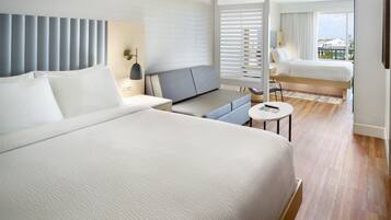 Een moderne hotelkamer met een groot bed, een sofa, een tafeltje en uitzicht op de stad door grote ramen.