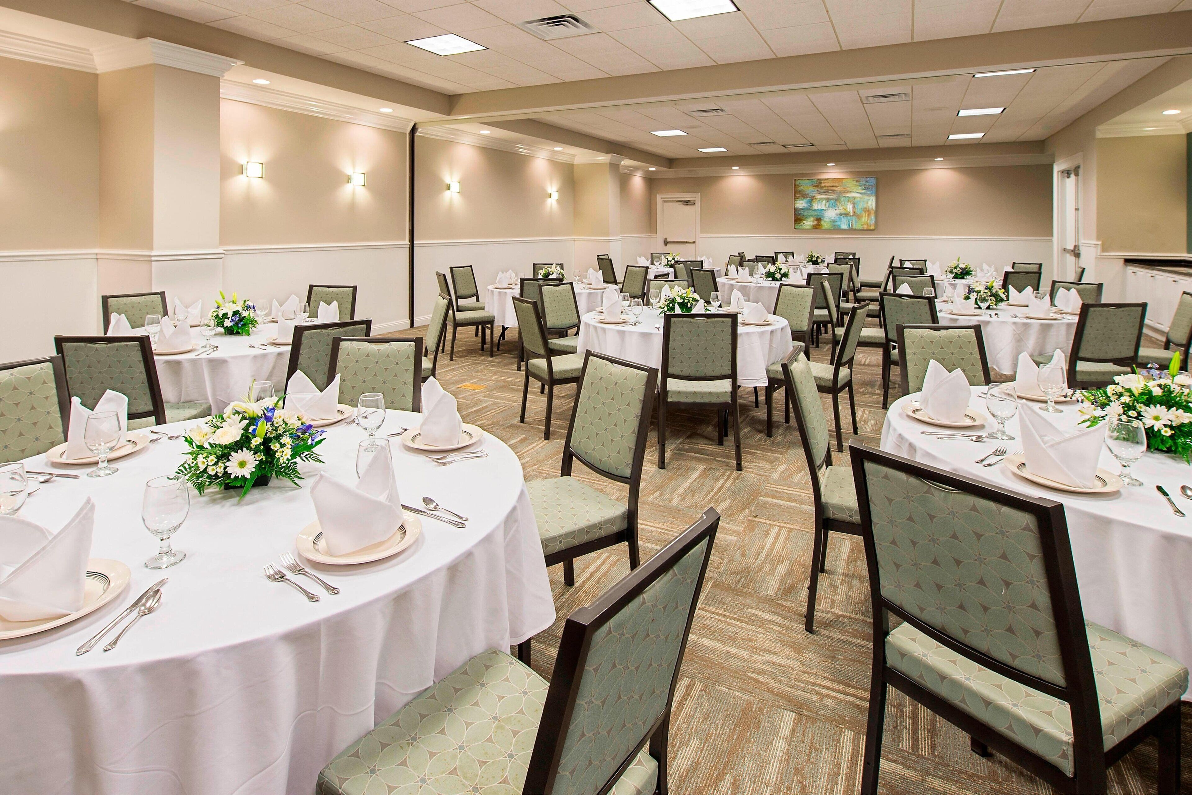 A conference room with multiple round tables set for dining, each with white tablecloths, chairs, and floral centerpieces.