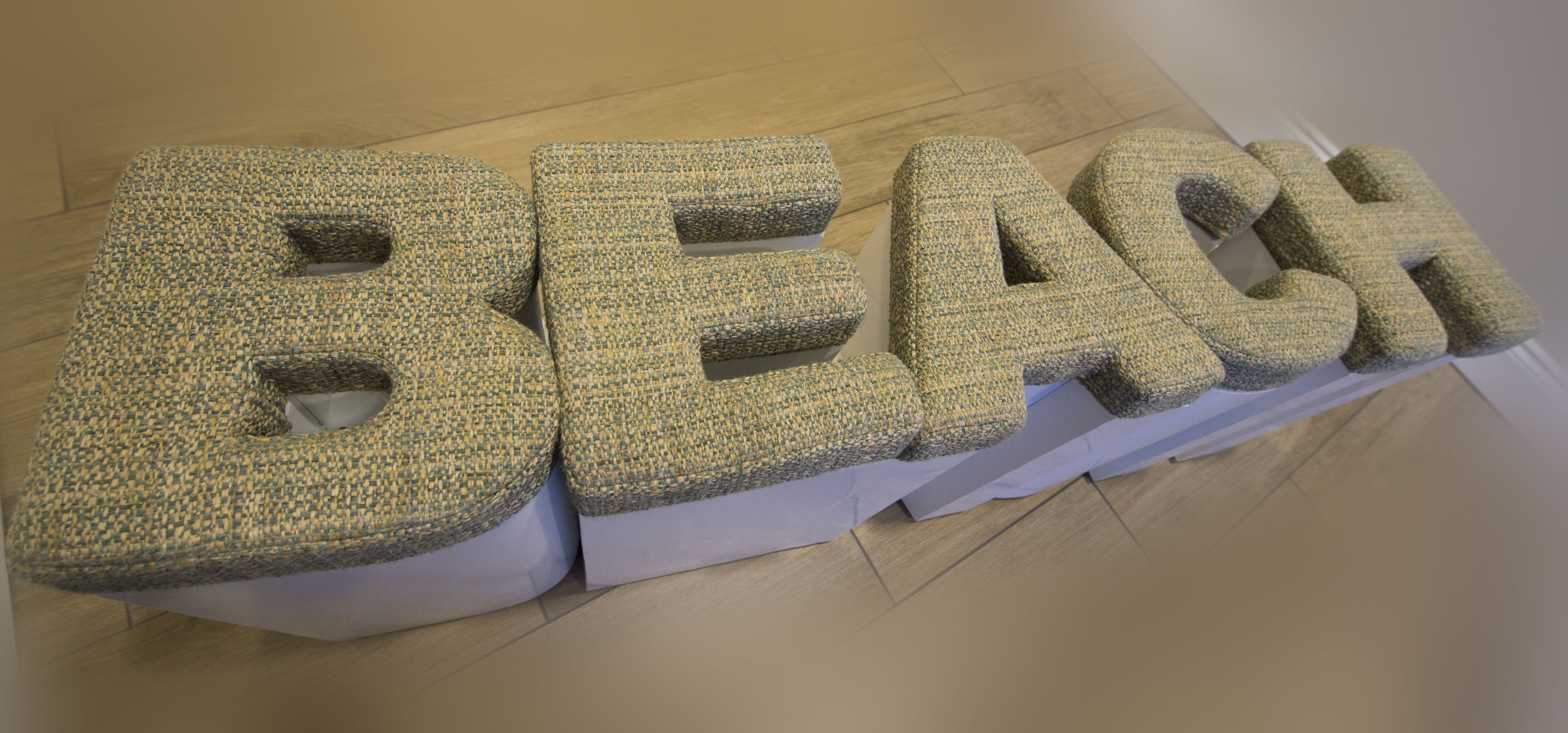 Une installation murale texturée formant le mot « PLAGE » avec de grandes lettres en relief.