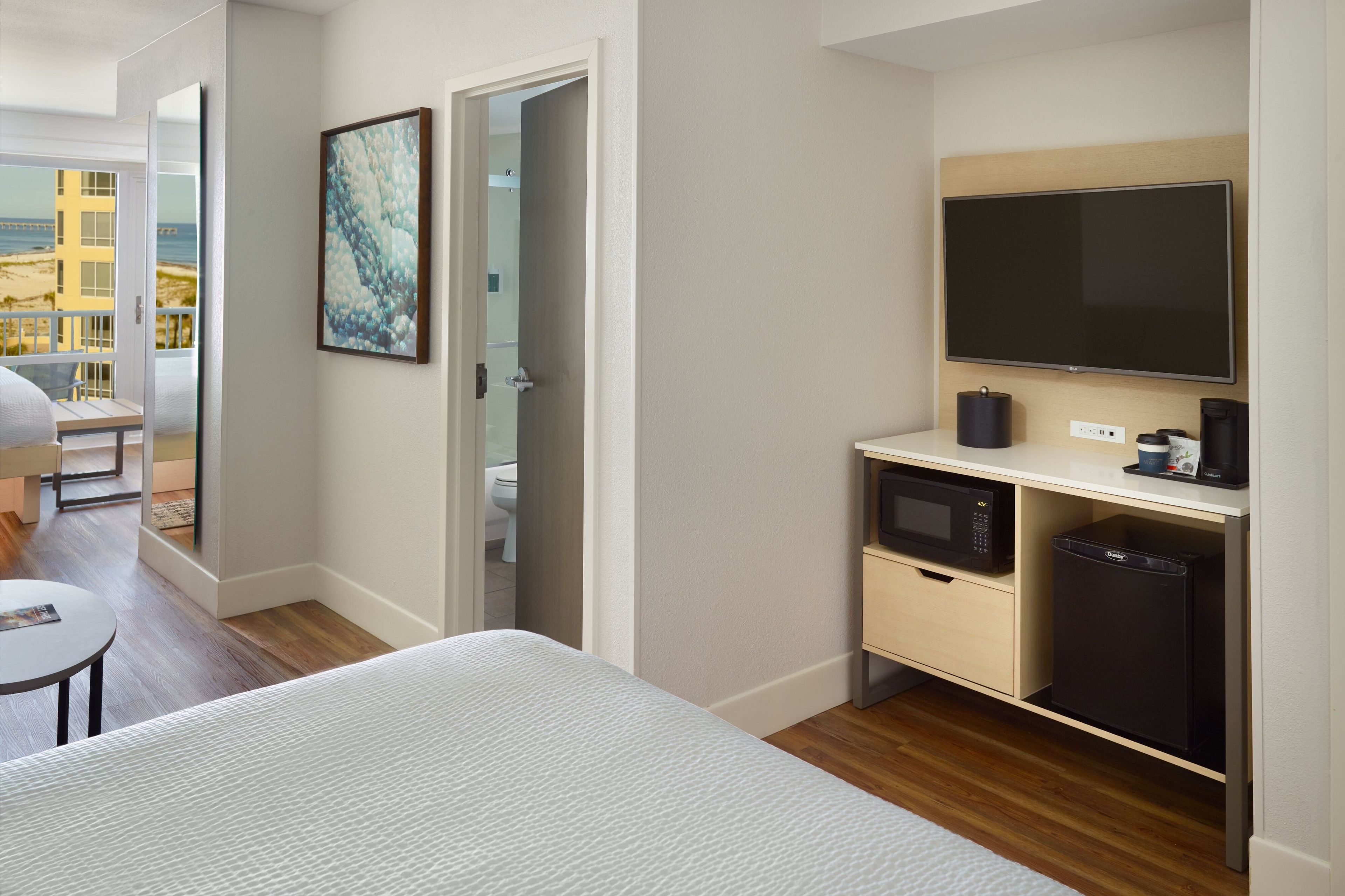 Een hotelkamer met een bed, een bureau met een flatscreen-televisie, een magnetron en een minibar.
