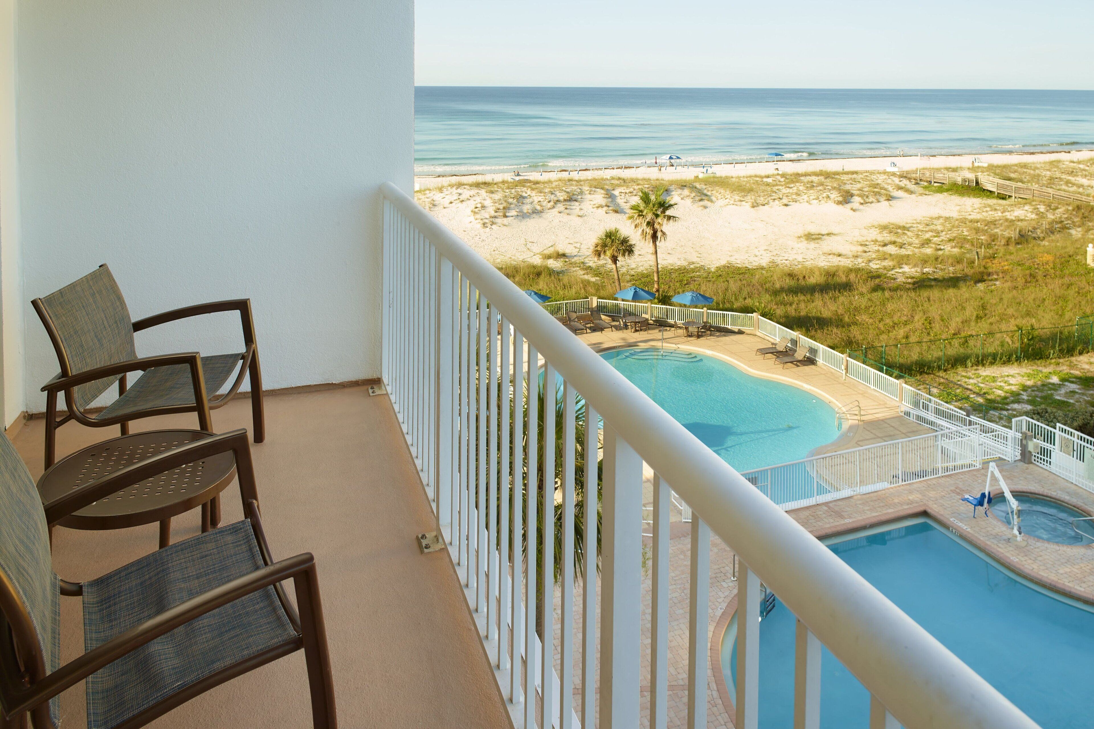 Een balkon met twee stoelen, een zwembad en uitzicht op het strand.