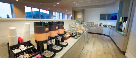Een ontbijtbuffet met koffieapparaten, een presentatie van fruit en een uitzicht op de stadshemel.