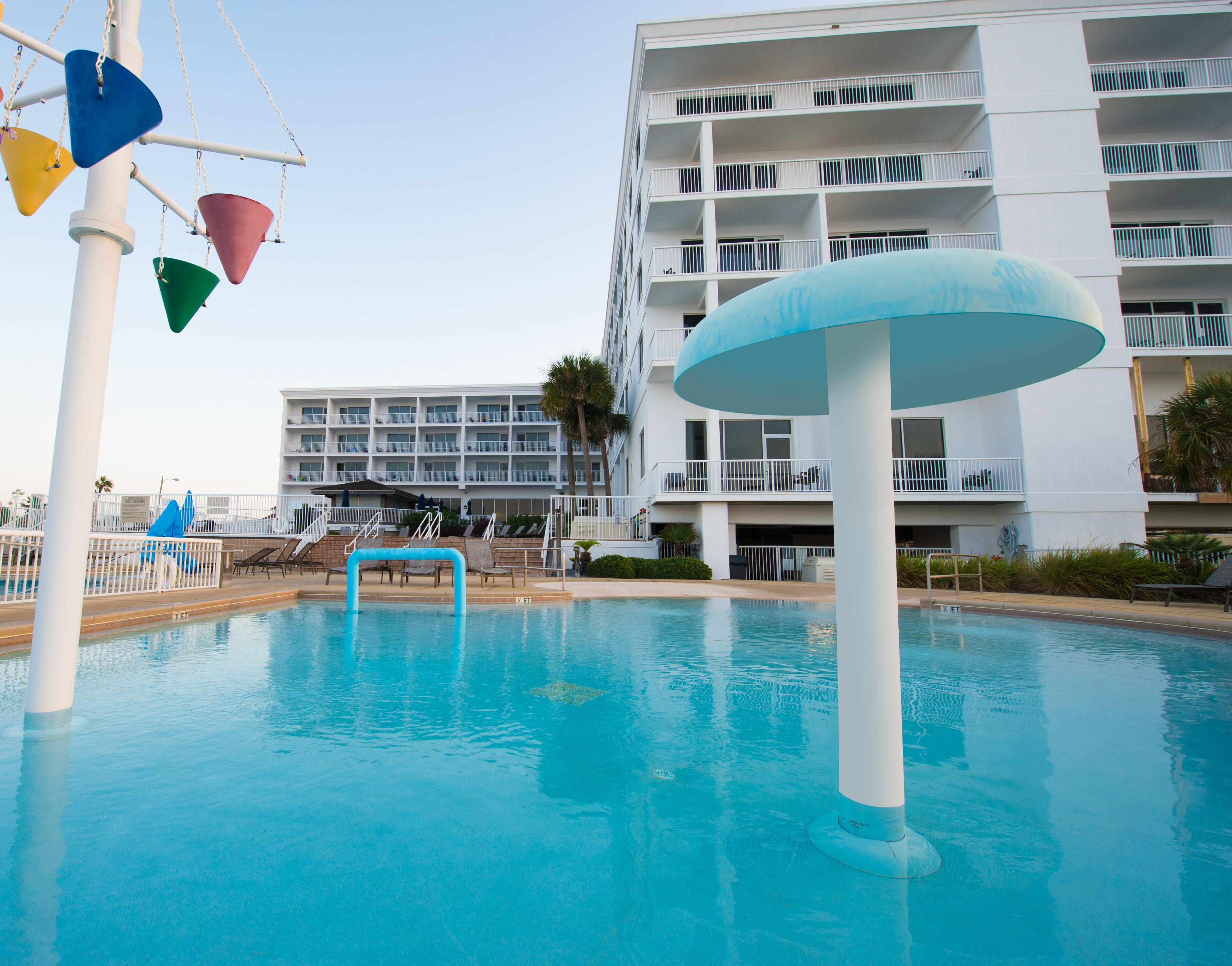 A swimming pool with a water slide, lounge chairs, and a multi-story building with balconies in the background.