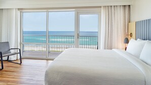A hotel room with a large bed, a chair, a view of the ocean through a sliding glass door, and a nightstand with a lamp. - SpringHill Suites Pensacola Beach (Pensacola Beach)
