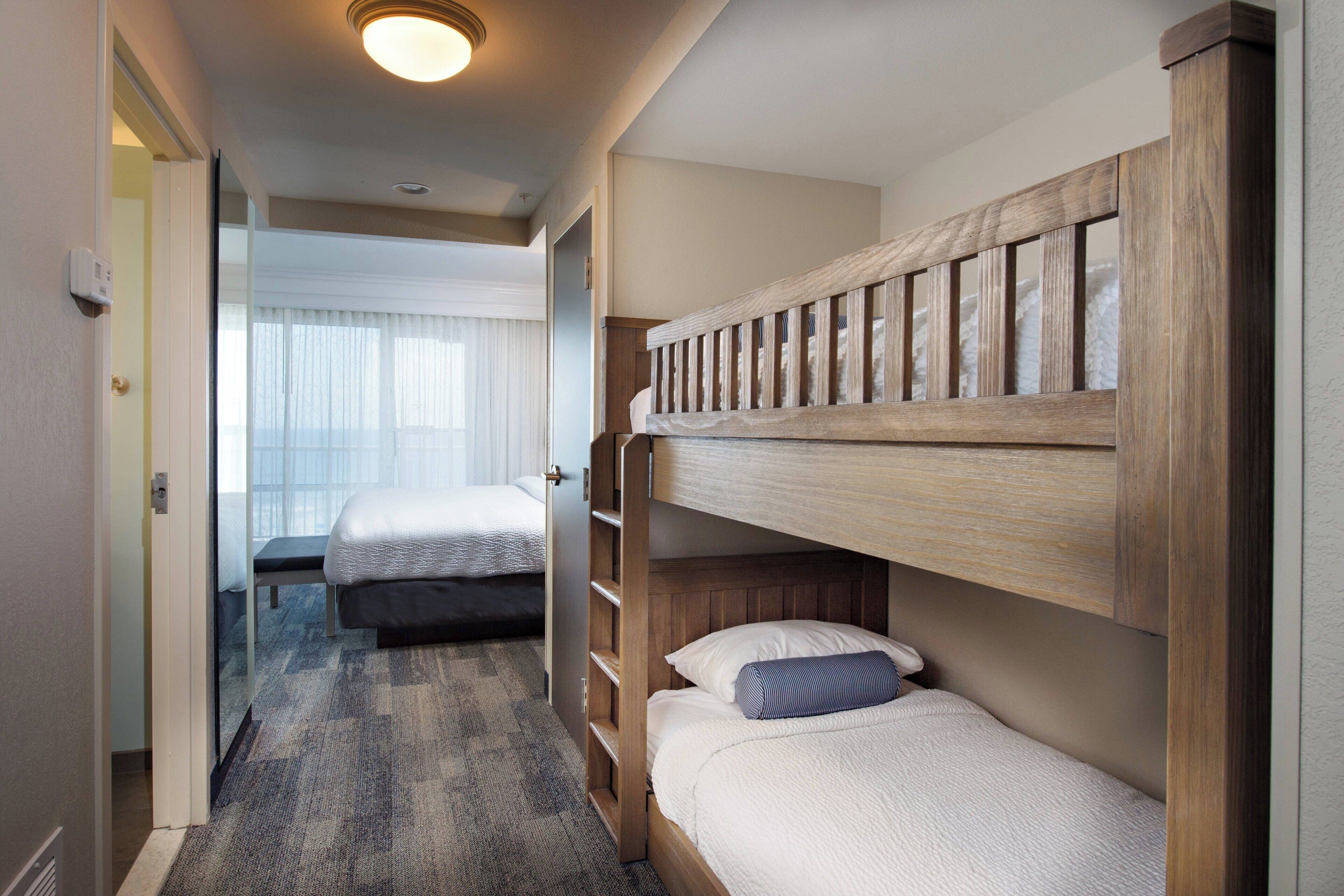 Une chambre d’hôtel avec deux lits superposés, un sol recouvert de moquette et une porte donnant sur une autre pièce.