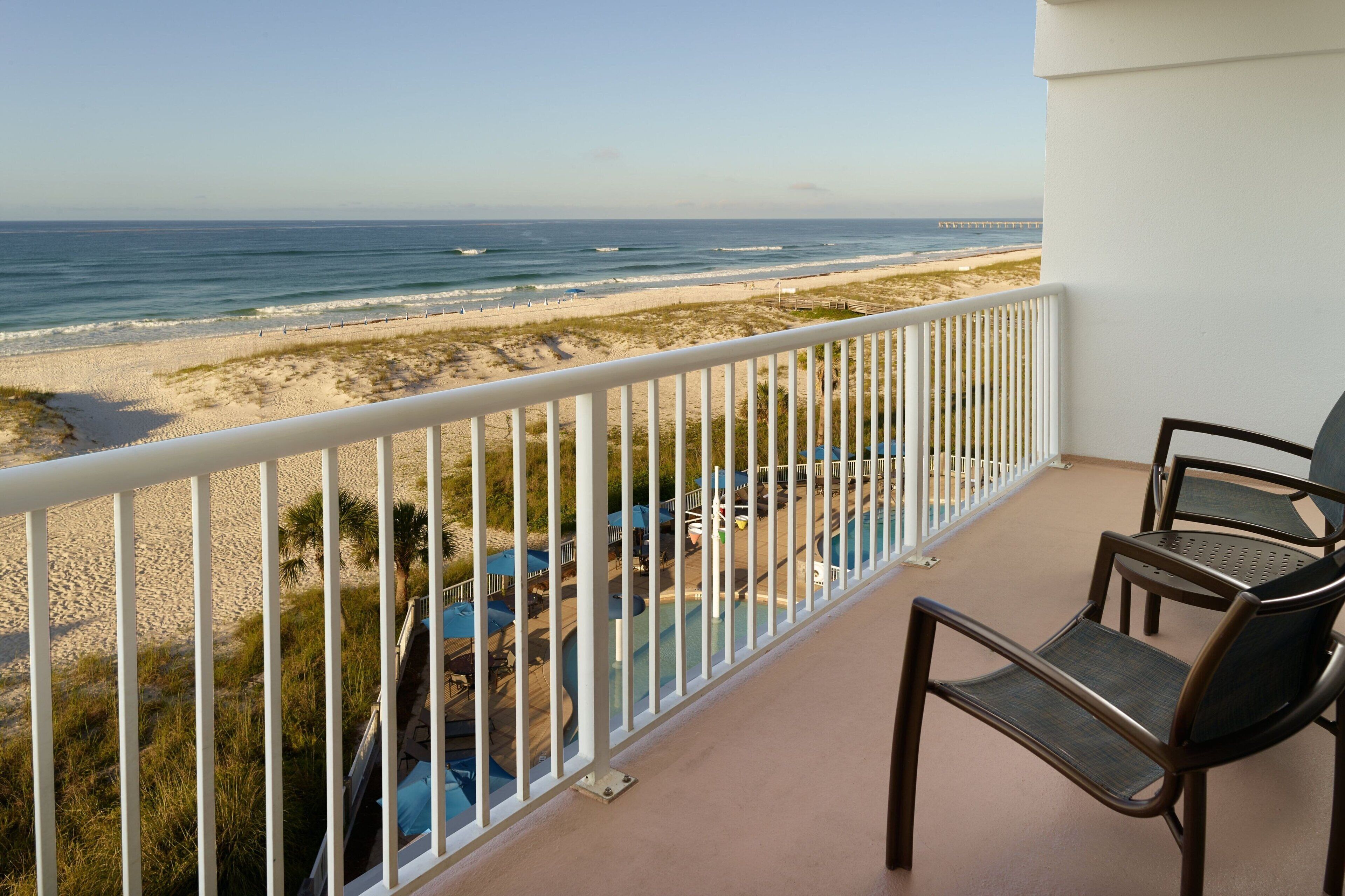 Ein Balkon mit Blick auf den Strand und den Ozean. Stühle und ein Poolbereich sind zu sehen.