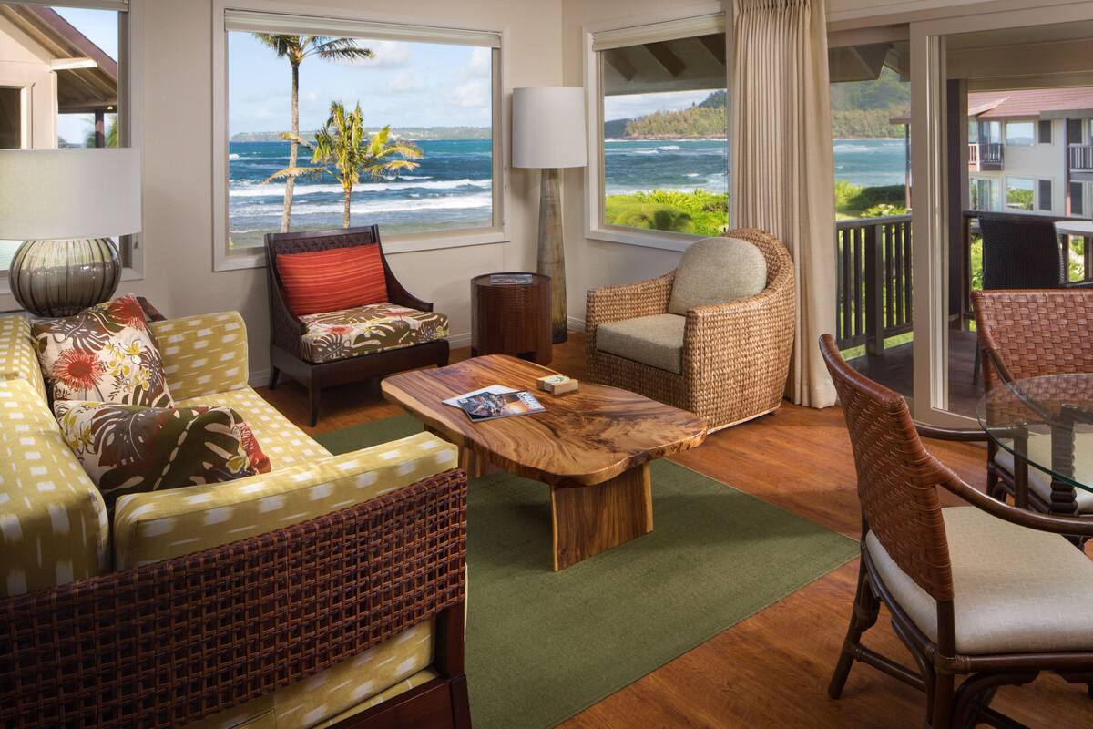 A cozy living room with wicker furniture, a wooden coffee table, and large windows offering ocean views.