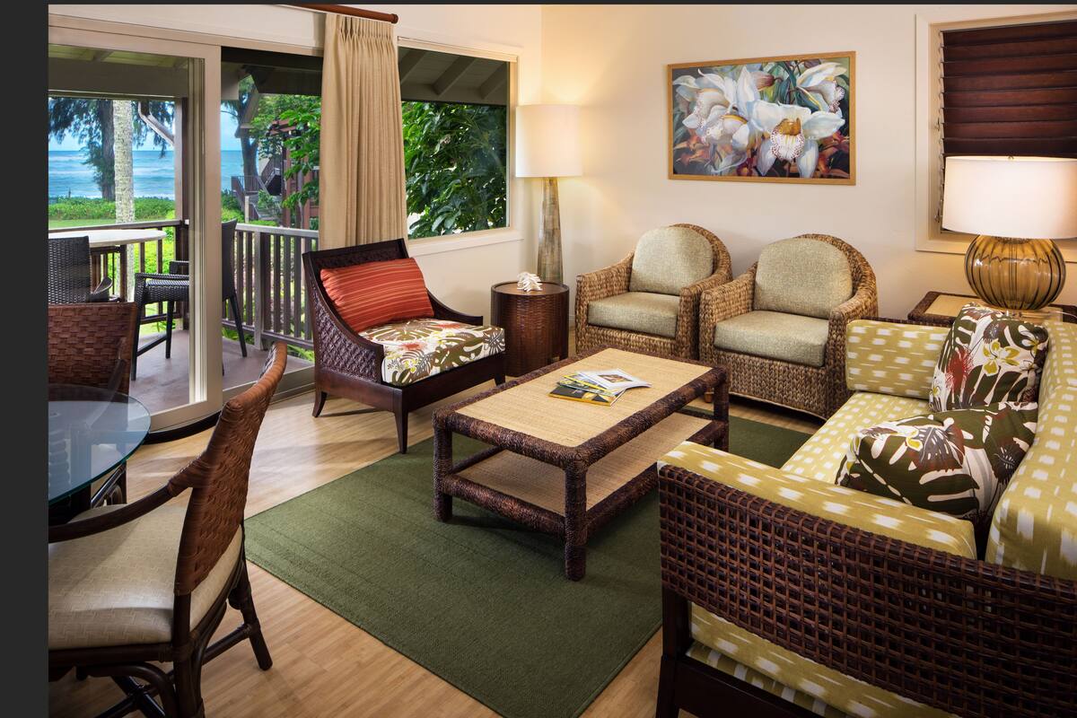 A living room with wicker furniture, a glass table, and a view of the ocean.