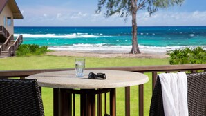 Une table ronde sur laquelle sont posés un verre d’eau et des lunettes de soleil, donnant sur une plage avec des vagues et un arbre.