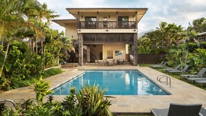 Une maison à deux étages dotée d’une piscine, d’un espace salon extérieur et d’une végétation tropicale luxuriante.