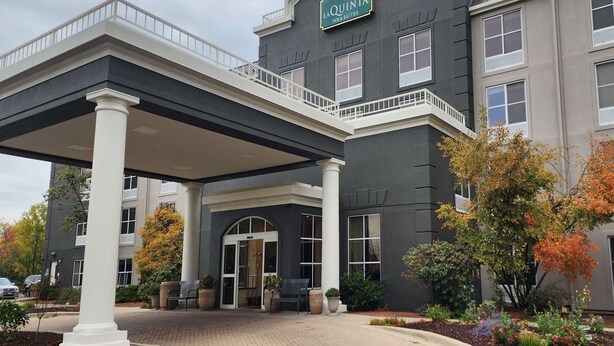 A hotel entrance with a covered walkway, a sign reading "La Quinta Inn Suites," and a landscaped area with trees and plants.