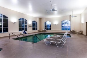 Una amplia piscina cubierta con paredes de vidrio transparente, varios ventiladores de techo y sillones de descanso alrededor de la zona de la piscina.