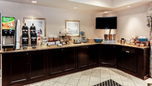 A hotel kitchen with a buffet setup, including coffee machines, a TV, and various food items.