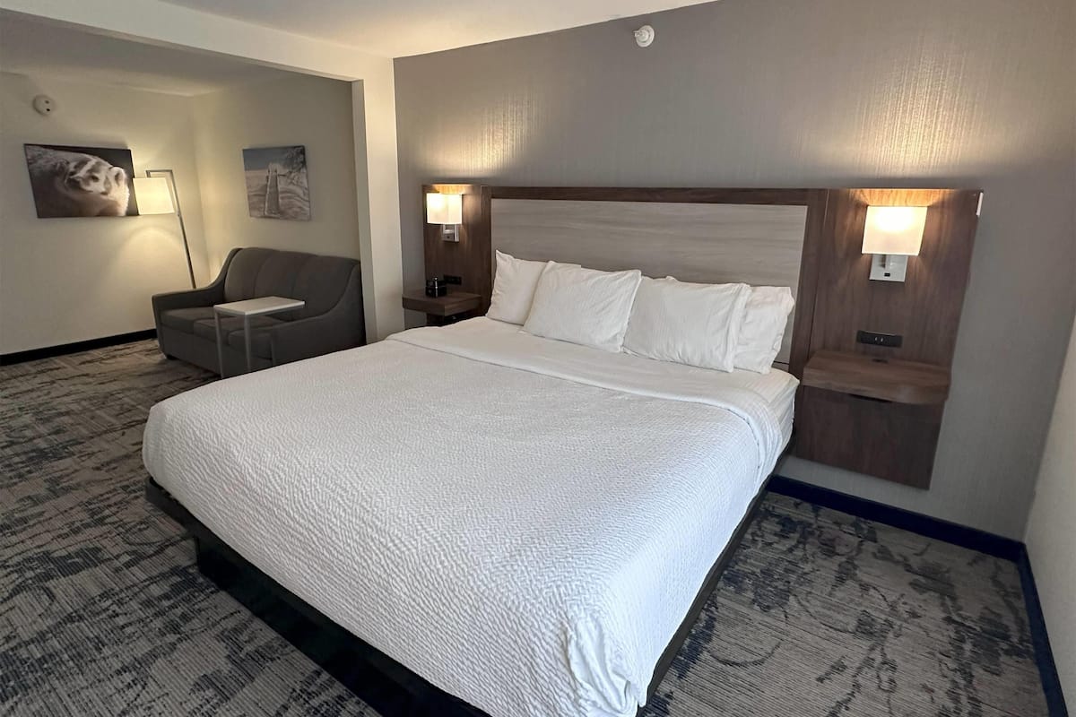 A hotel room with a large bed, a chair, and two bedside tables with lamps.