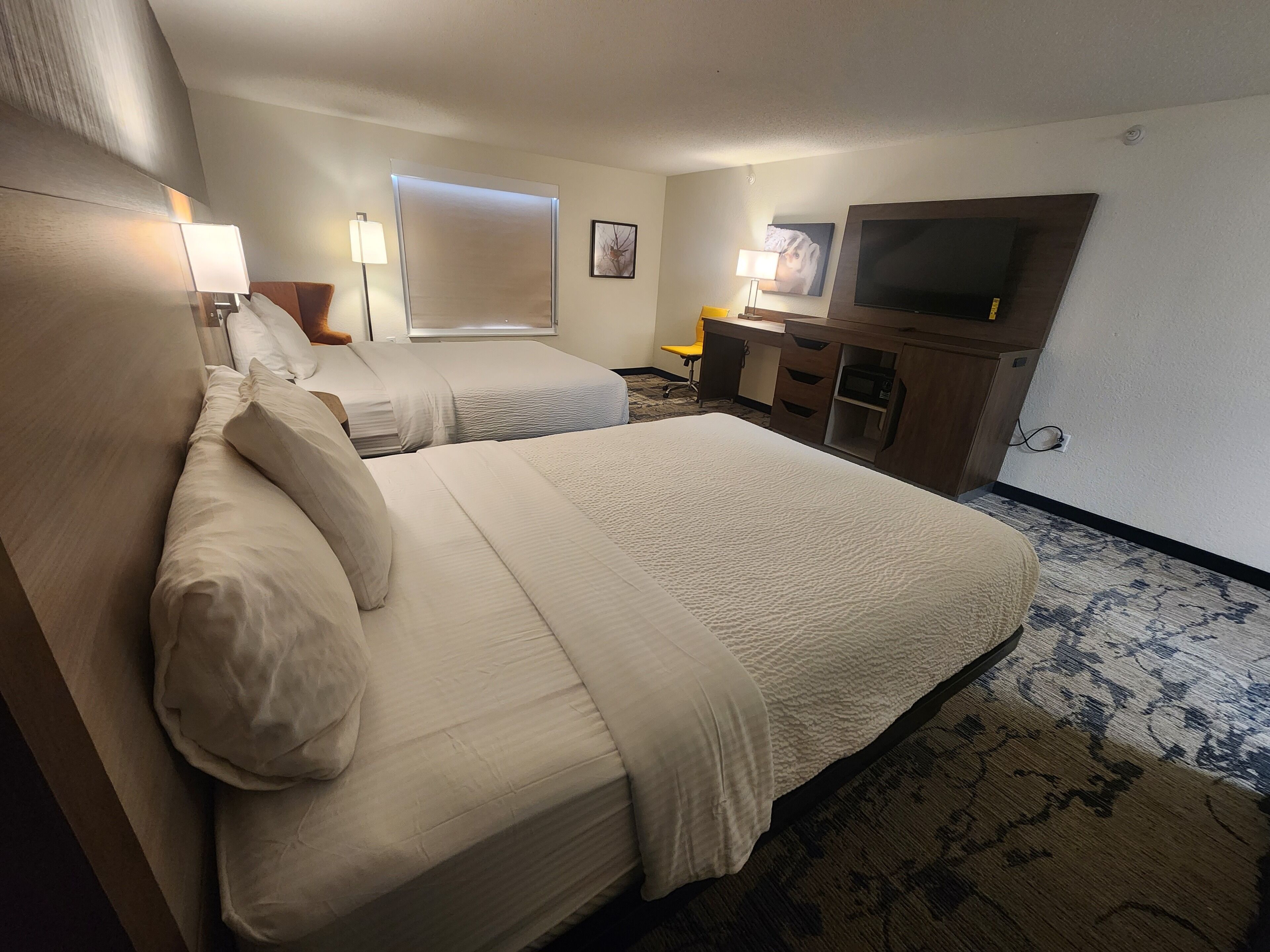 A hotel room with two beds, a desk, a television, and a window with blinds.