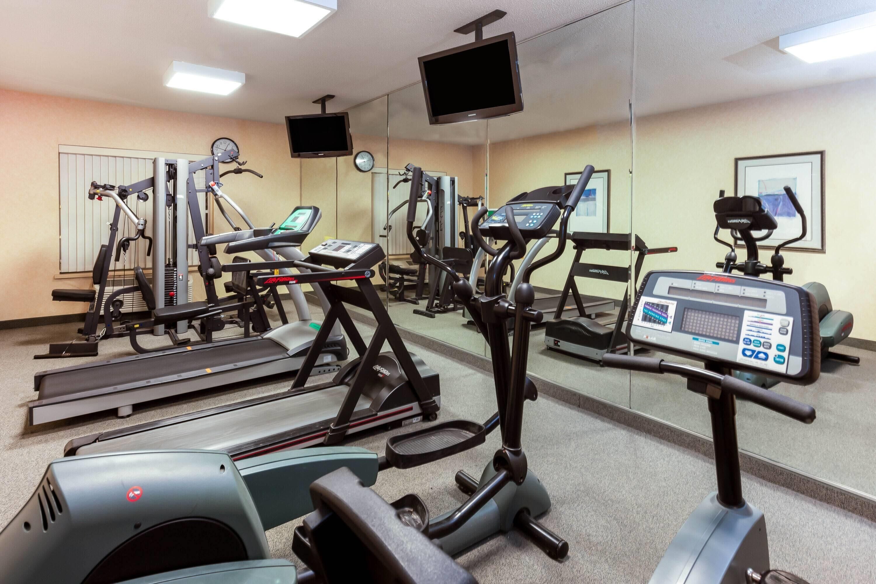 Ein Fitnessstudio mit unterschiedlichen Trainingsgeräten, darunter Laufbänder, Crosstrainer und Kraftgeräte.
