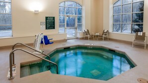 An indoor swimming pool with clear glass walls, a pool ladder, and several chairs around the pool area.