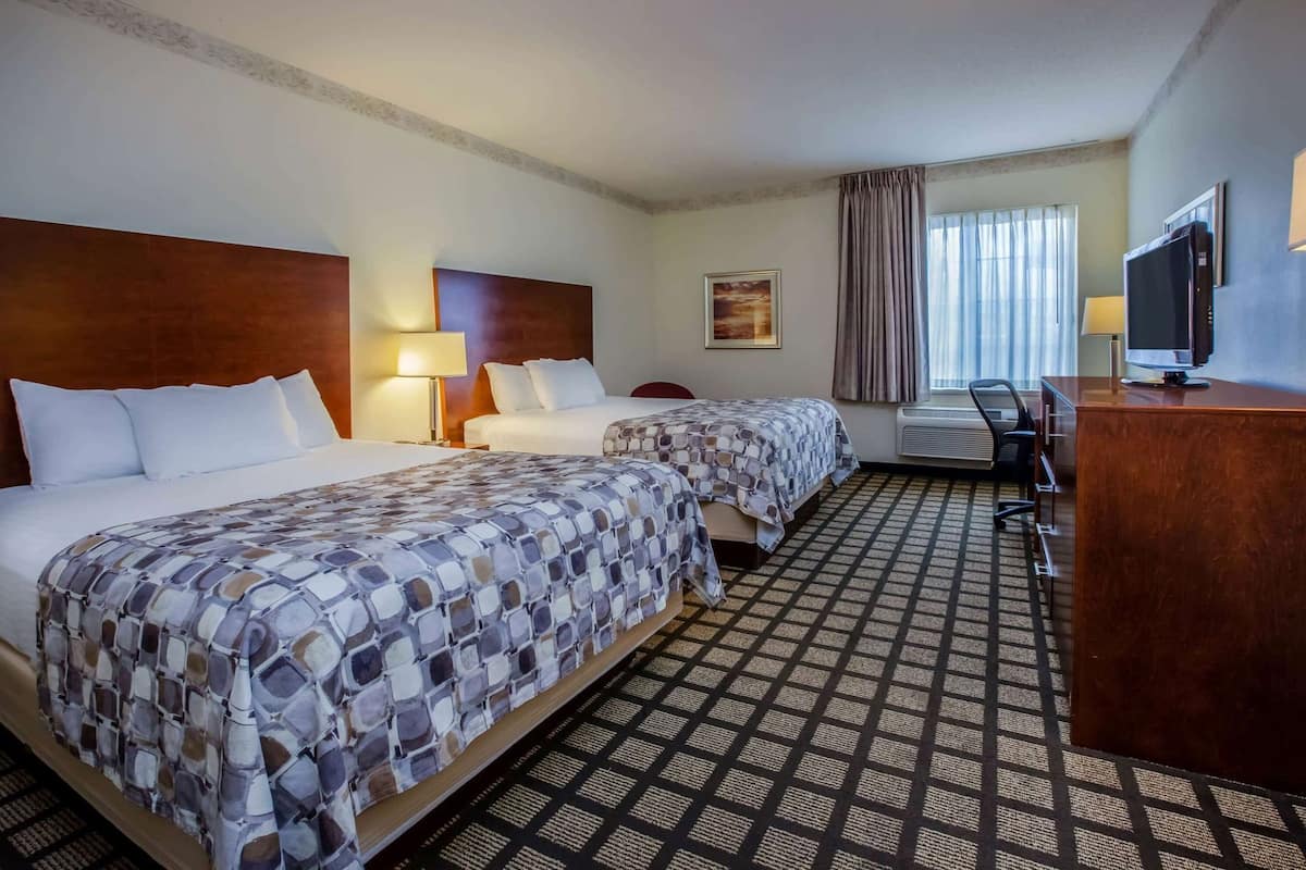 A hotel room with two beds, a desk, a television, and a window with curtains.