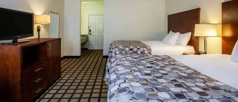 A hotel room with a television, a wooden dresser, a patterned bedspread, and a nightstand with a lamp.