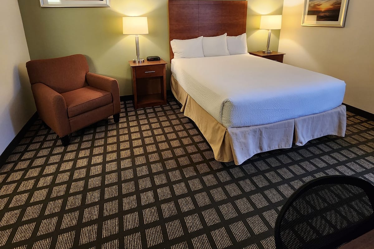 A hotel room with a bed, two bedside tables with lamps, a chair, and patterned carpet.