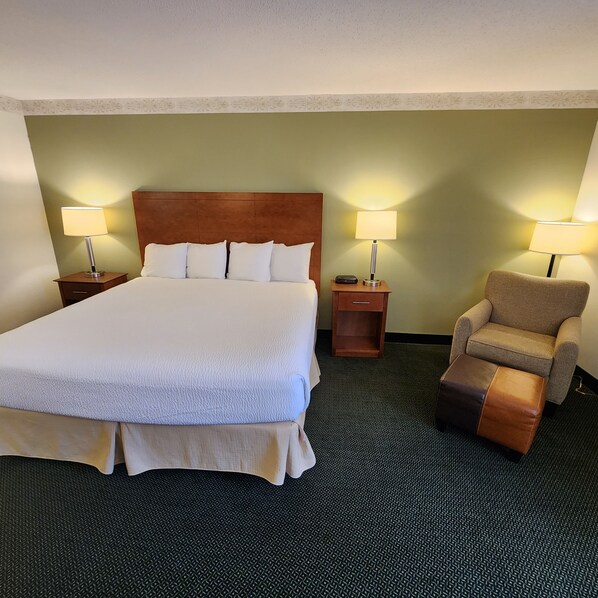 A hotel room with a large bed, two bedside tables with lamps, a chair, and a carpeted floor.