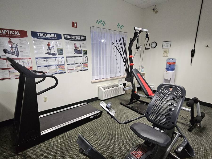 Academia com equipamentos de ginástica, incluindo esteira ergométrica, elíptico e banco de musculação.