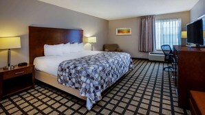 A hotel room with a large bed, a desk with a television, a chair, and a window with curtains.