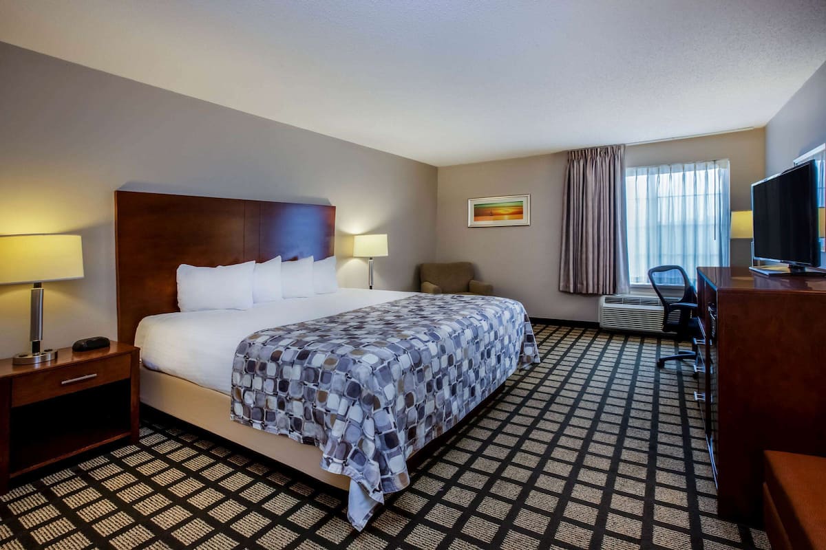 A hotel room with a large bed, a desk with a television, a chair, and a window with curtains.