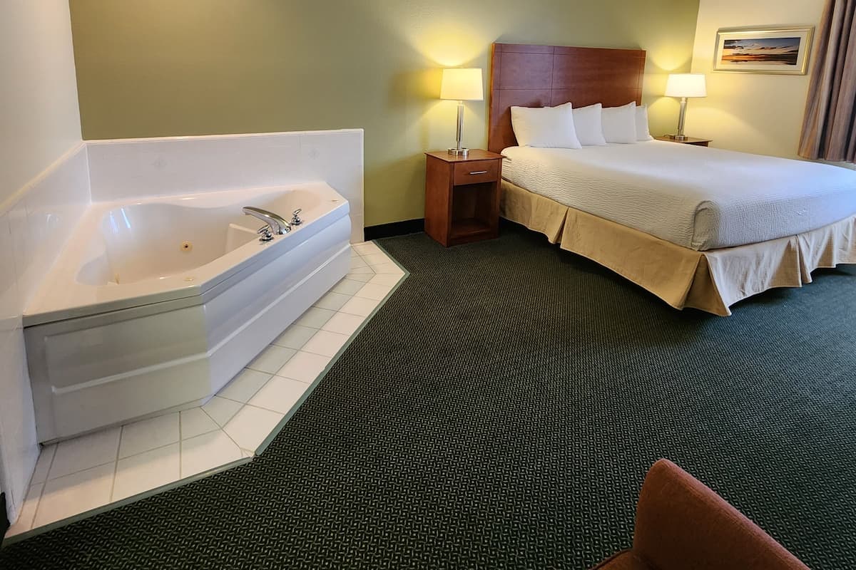 A hotel room with a large bathtub, a bed with white linens, two bedside lamps, and a ceiling fan.