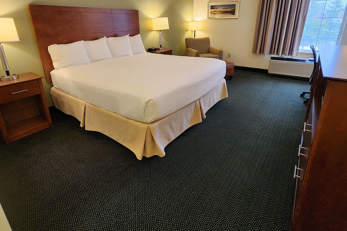 A hotel room with a large bed, two bedside tables, a chair, a desk, and a window with curtains.