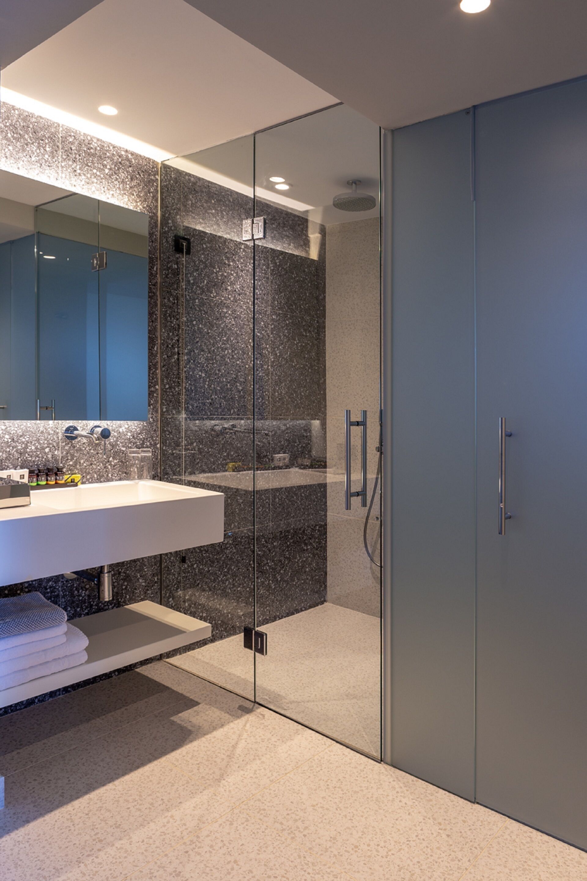 Un baño moderno con ducha de vidrio, lavamanos blanco y un espejo grande.