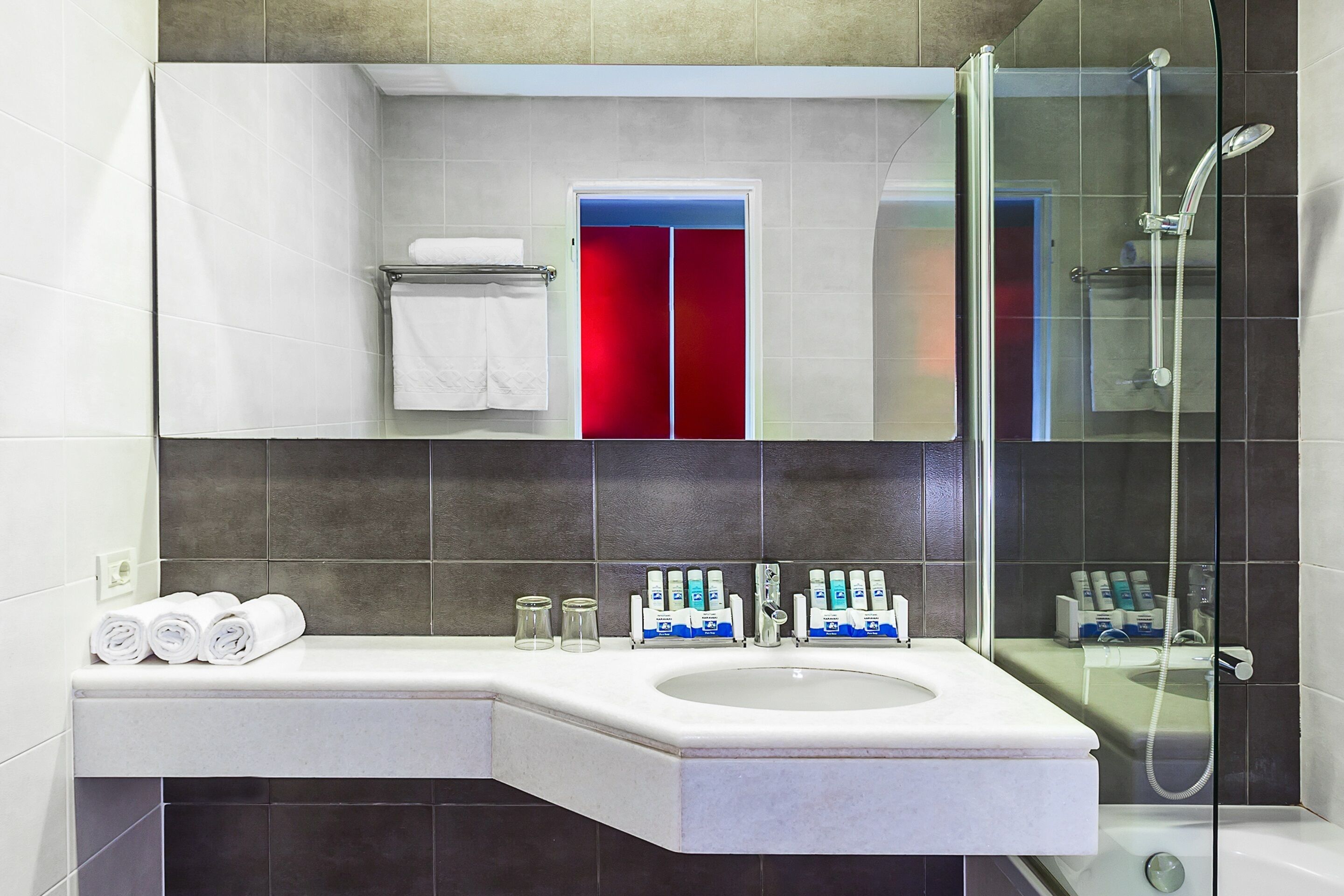A modern bathroom with a large sink, mirror, and glass-enclosed shower.