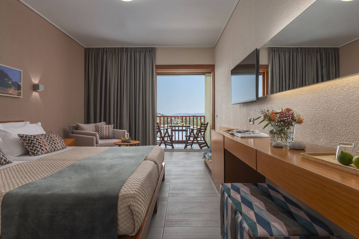 Une chambre d’hôtel comprenant un lit, un canapé, une table à manger avec des chaises, un balcon avec vue et une salle de bain avec un miroir et un lavabo.