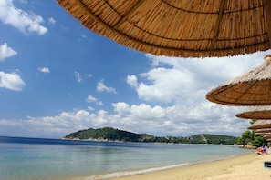 Una spiaggia con acque cristalline, una riva sabbiosa e un gazebo con tetto di paglia.