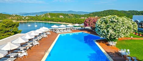 A poolside area with lounge chairs and umbrellas, a large pool, and a view of the lake and hills.