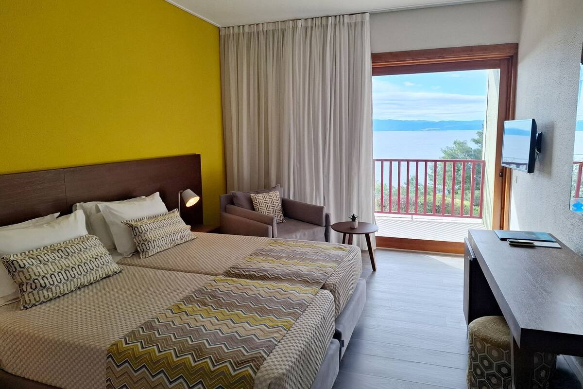 Une chambre d’hôtel avec un lit, un canapé, une petite table, une télévision et un balcon avec vue.