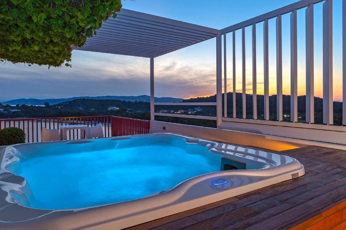 Un bain à remous sur une terrasse en bois, avec vue sur les collines et un coucher de soleil.