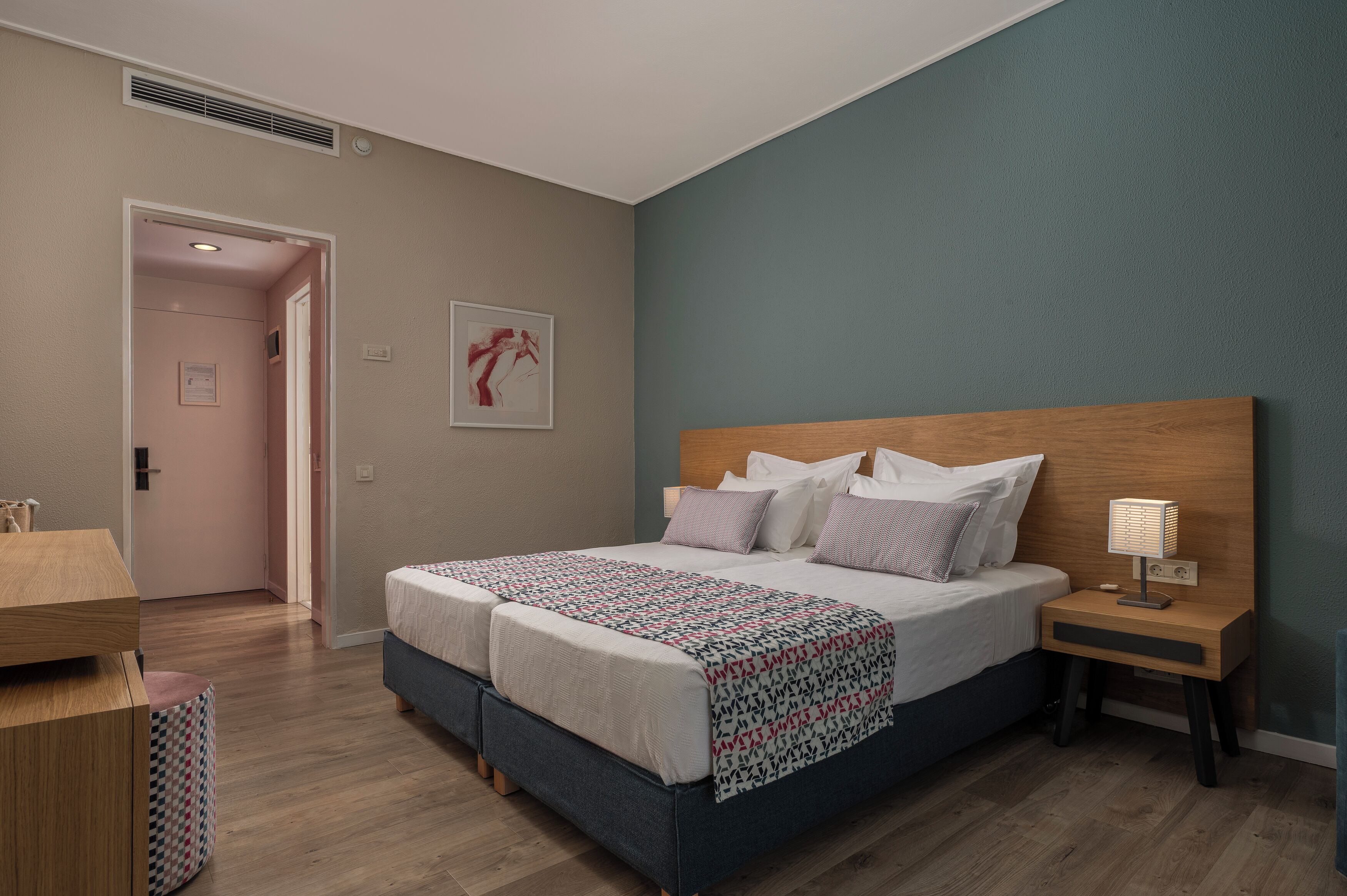 A bedroom with a double bed, bedside tables, a nightstand, a wooden headboard, and a wall-mounted artwork.