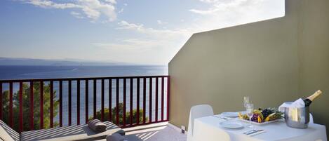 A balcony with a white table set for two, a bottle of champagne, and a fruit platter.