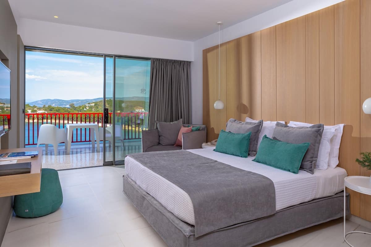 Une chambre moderne avec un grand lit, un bureau et un balcon doté d’une rambarde rouge.