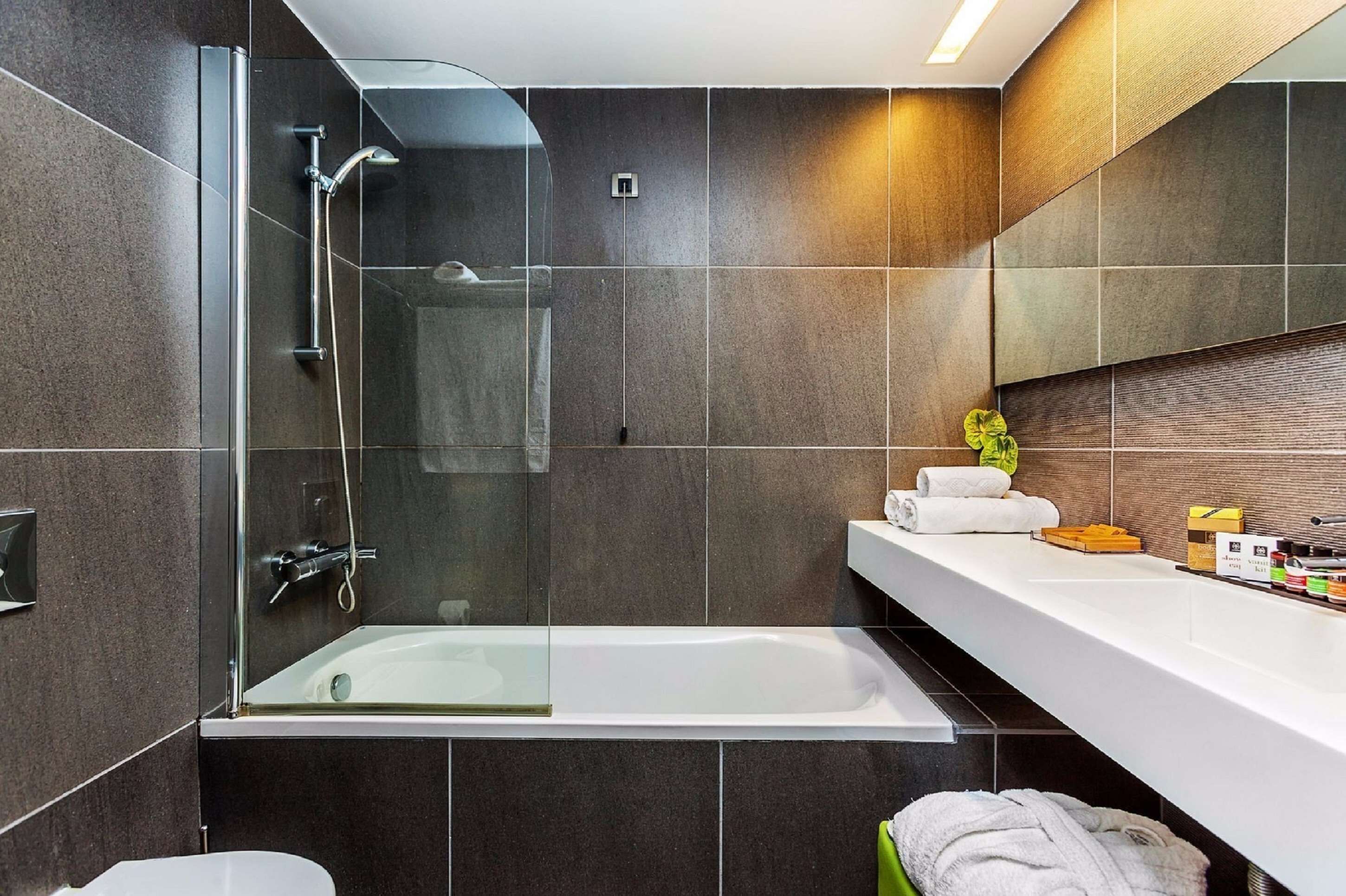 A modern bathroom with a glass-enclosed shower, a white bathtub, and a vanity with toiletries.