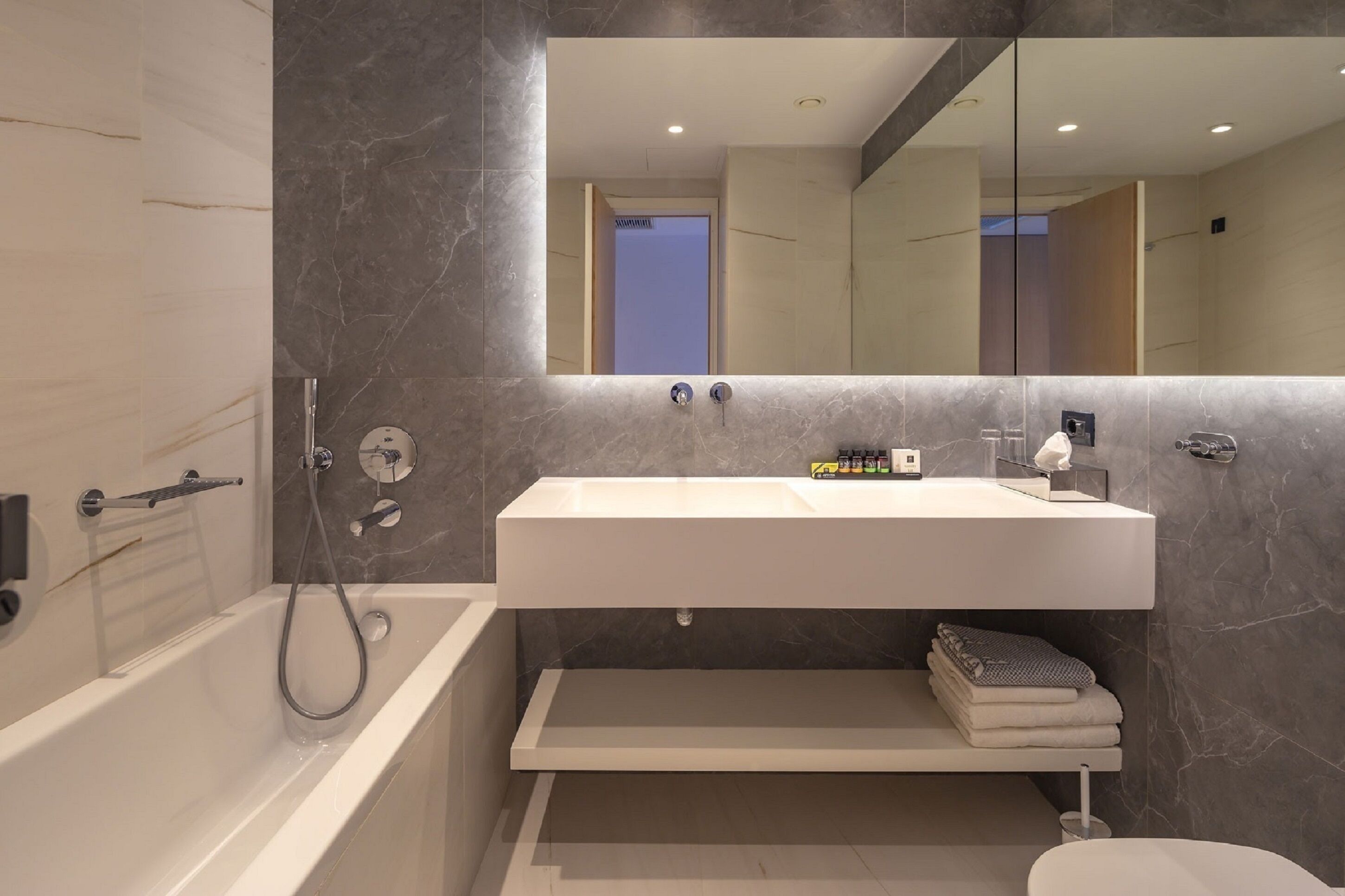 Ein modernes Badezimmer mit einer weißen Badewanne, einem großen Spiegel und einem weißen Waschbecken.