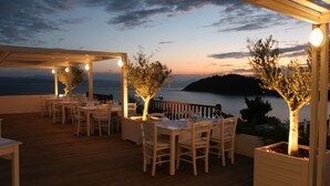 An outdoor dining area with tables and chairs, a pergola, and trees. - Skiathos Palace Hotel (Skiathos)