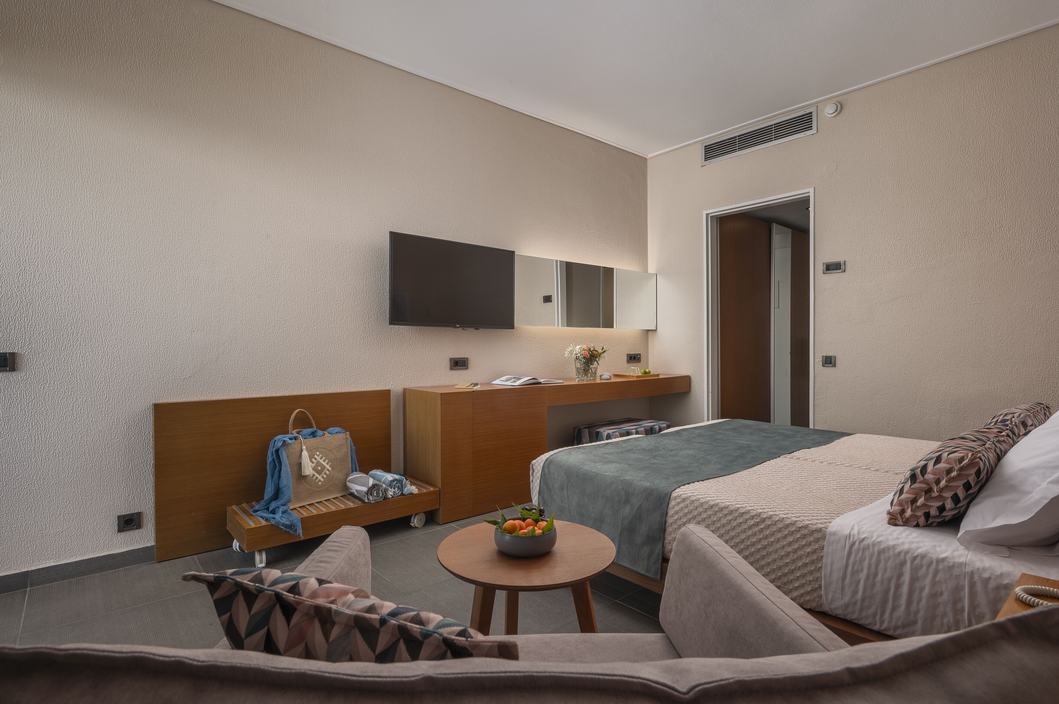 Une chambre d’hôtel équipée d’un lit, d’un bureau, d’une chaise, d’une petite table sur laquelle se trouve un saladier rempli de fruits, et d’un téléviseur fixé au mur.