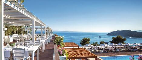 A seaside restaurant with outdoor seating, a pool, and a view of the ocean.