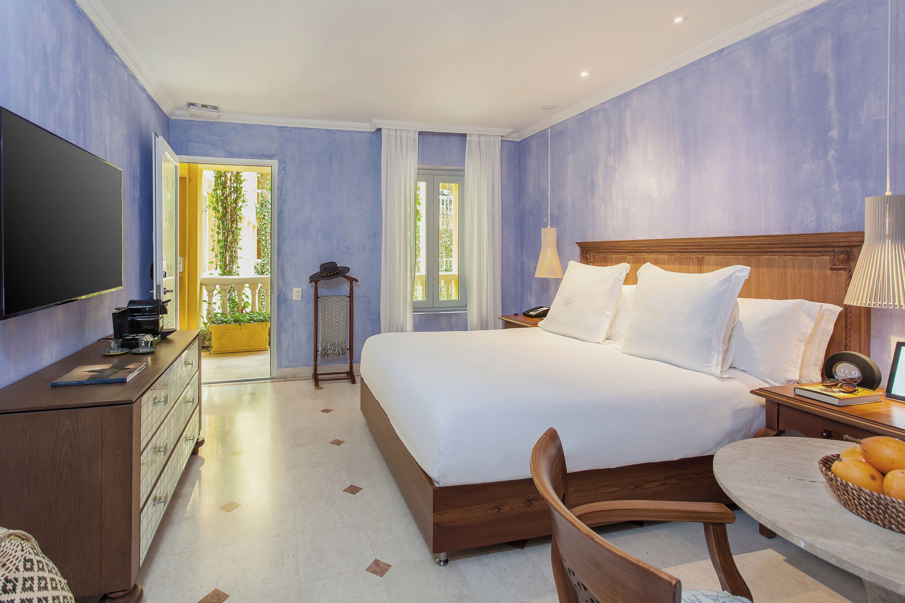 A bedroom with a bed, bedside table, lamp, TV, dresser, and a view of the outdoors.