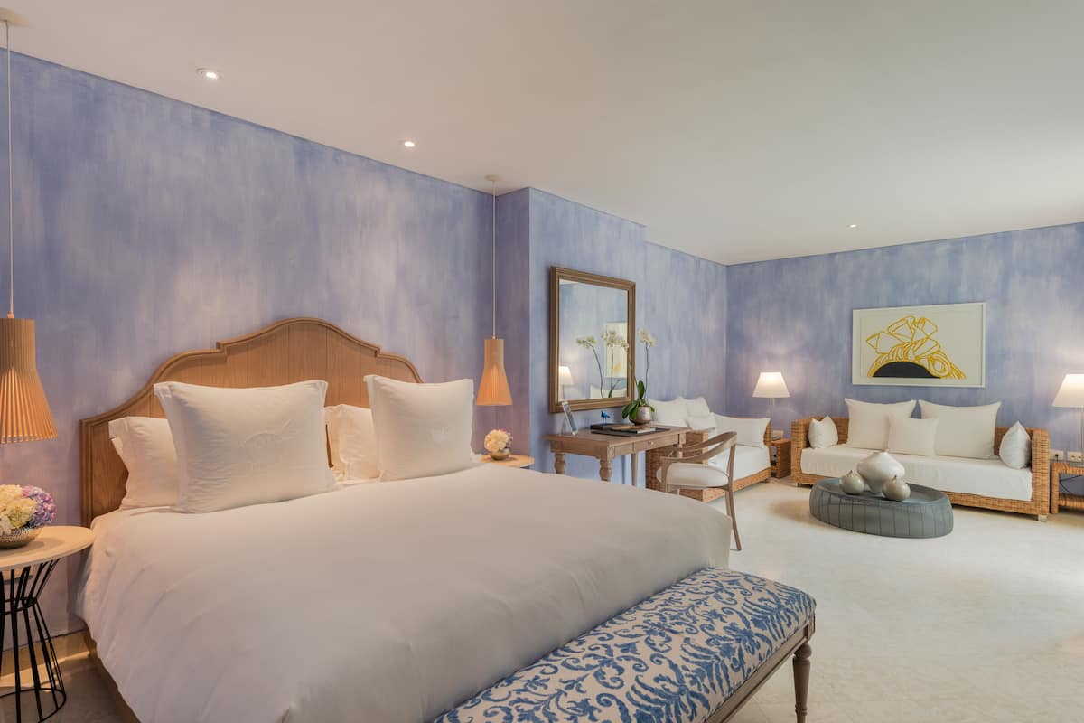 Een hotelkamer met een groot bed, een bank, een klein tafeltje met een lamp en een spiegel aan de muur.