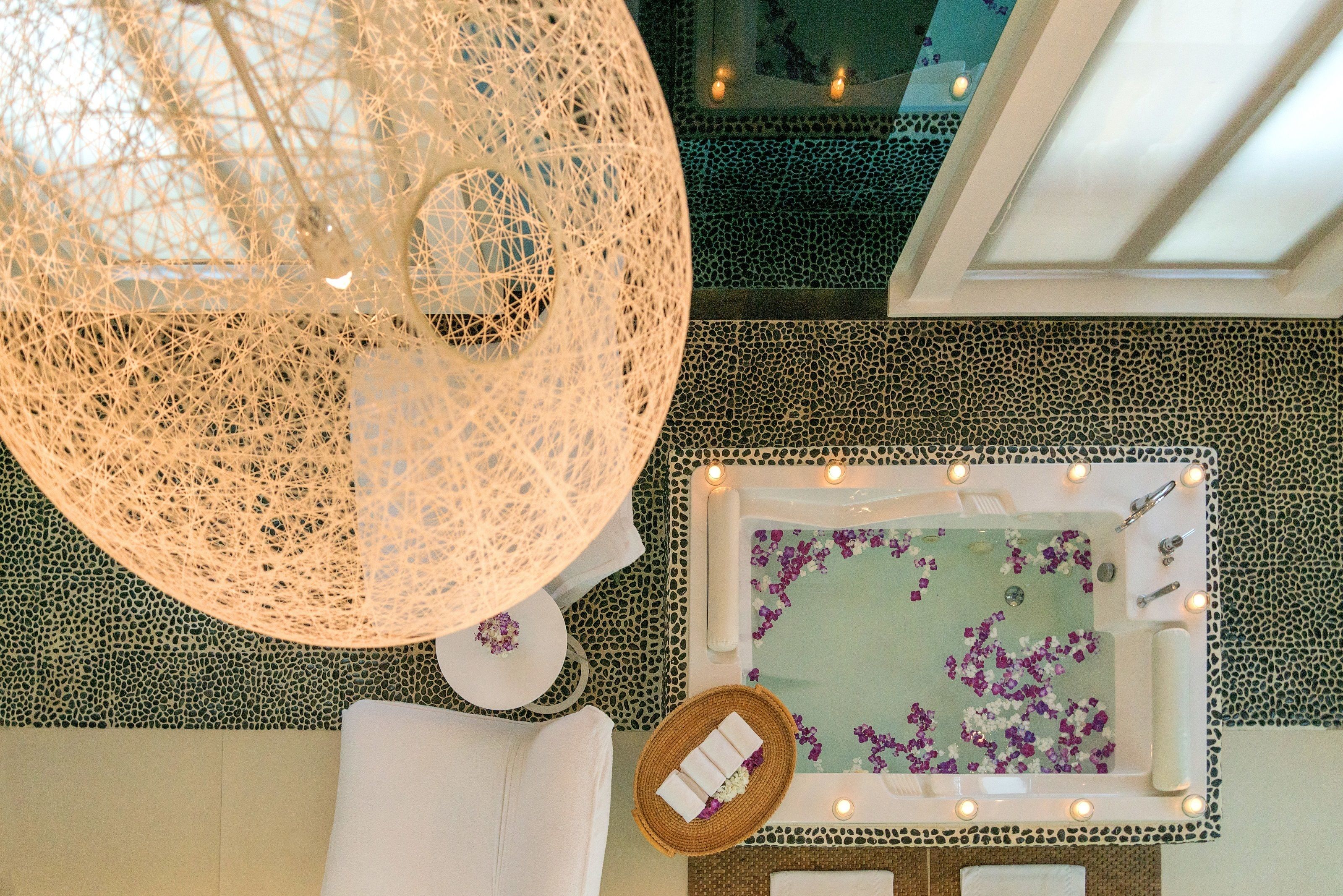 A spa area with a hot tub surrounded by lights, a woven light fixture, and a patterned floor.