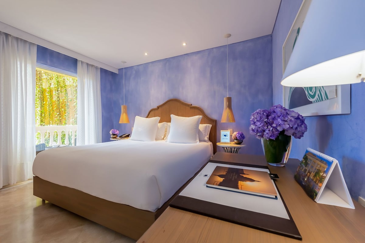 Habitación de hotel con una cama grande, mesitas de noche, cortinas y vistas a zonas verdes.